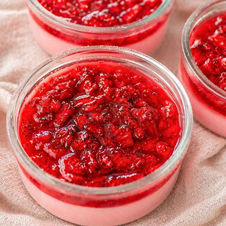 Strawberry pudding in a glass topped with chunky homemade strawberry jam, with extra pudding cups in the background.