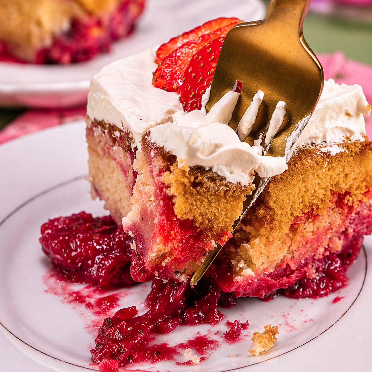 Fork cutting into a slice of strawberry shortcut cake with creamy frosting and fresh strawberry topping, revealing moist vanilla cake layers and juicy strawberry filling on a white plate.