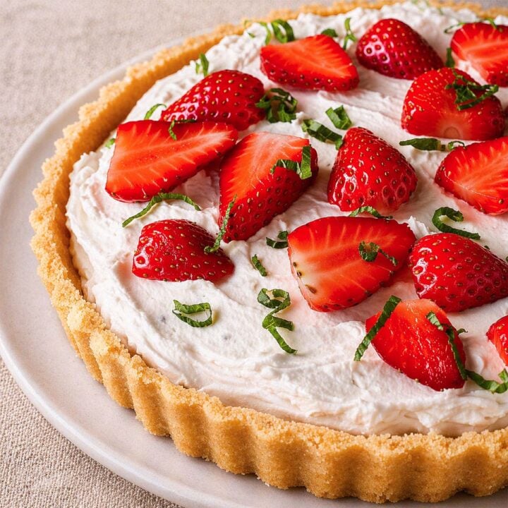 No-bake strawberry tart in a fluted tart pan with creamy filling, fresh strawberry halves, and mint leaves