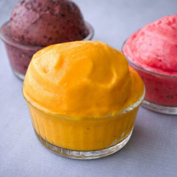 sugar free frozen yogurt scoop in a glass ramekin with berry and strawberry frozen yogurt in the background on a light linen surface