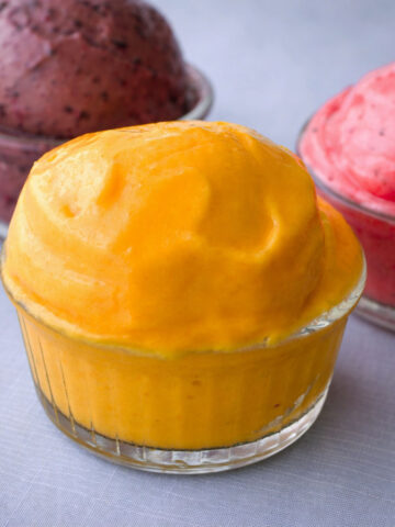 sugar free frozen yogurt scoop in a glass ramekin with berry and strawberry frozen yogurt in the background on a light linen surface