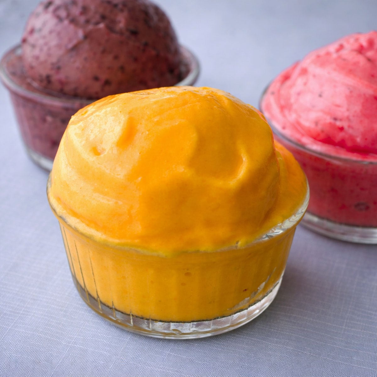 sugar free frozen yogurt scoop in a glass ramekin with berry and strawberry frozen yogurt in the background on a light linen surface