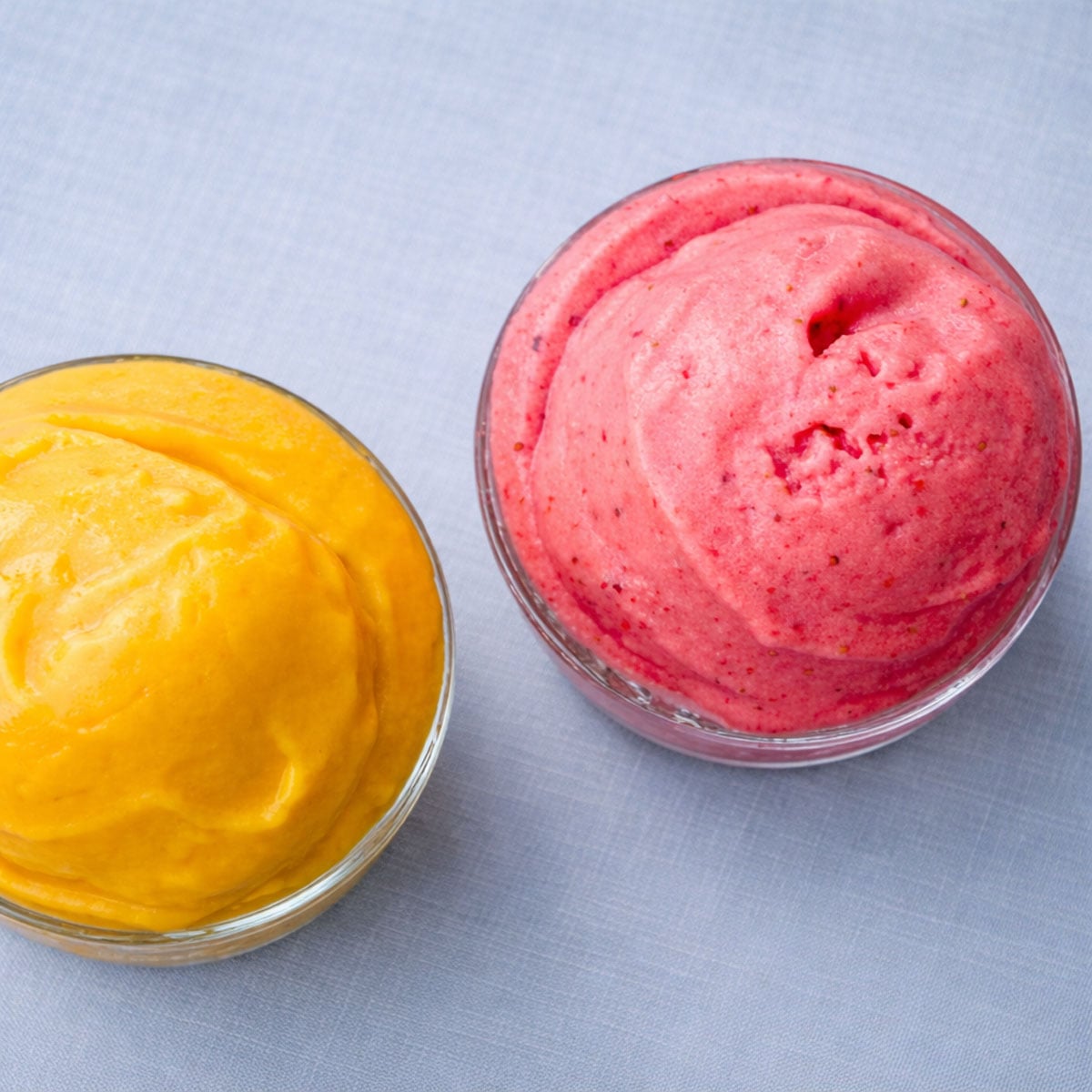 top view of sugar free frozen yogurt with mango and strawberry flavors in small glass bowls on a light linen background