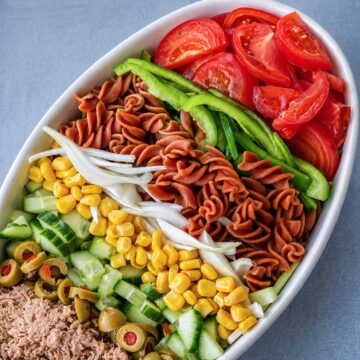 Tuna pasta salad with tomatoes, green peppers, corn, cucumber, olives, onion, and rotini pasta arranged in a white bowl