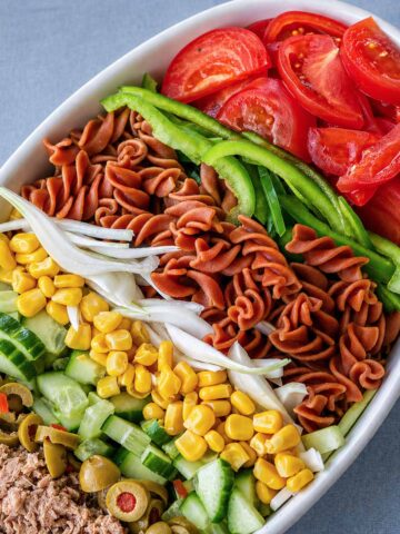 Tuna pasta salad with tomatoes, green peppers, corn, cucumber, olives, onion, and rotini pasta arranged in a white bowl