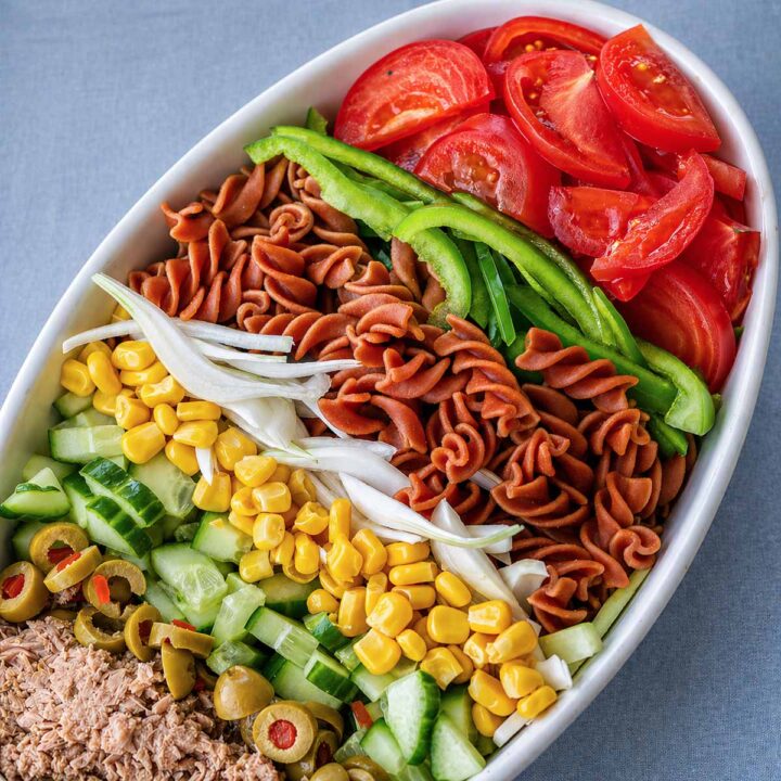 Tuna pasta salad with tomatoes, green peppers, corn, cucumber, olives, onion, and rotini pasta arranged in a white bowl