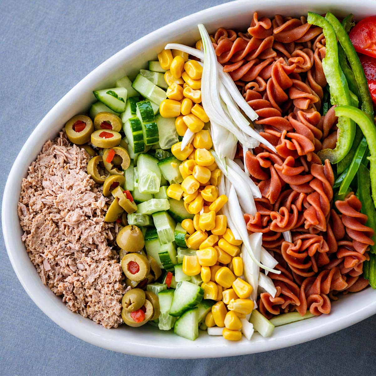 Close up Tuna pasta salad with tomatoes, green peppers, corn, cucumber, olives, onion, and rotini pasta arranged in a white bowl