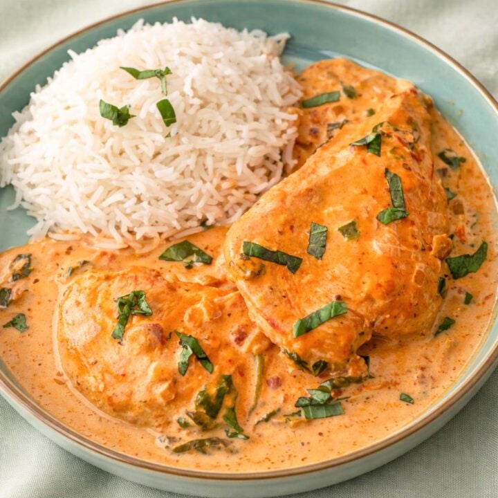 Tuscan chicken in creamy sun-dried tomato sauce served with white rice on a plate, garnished with fresh herbs.