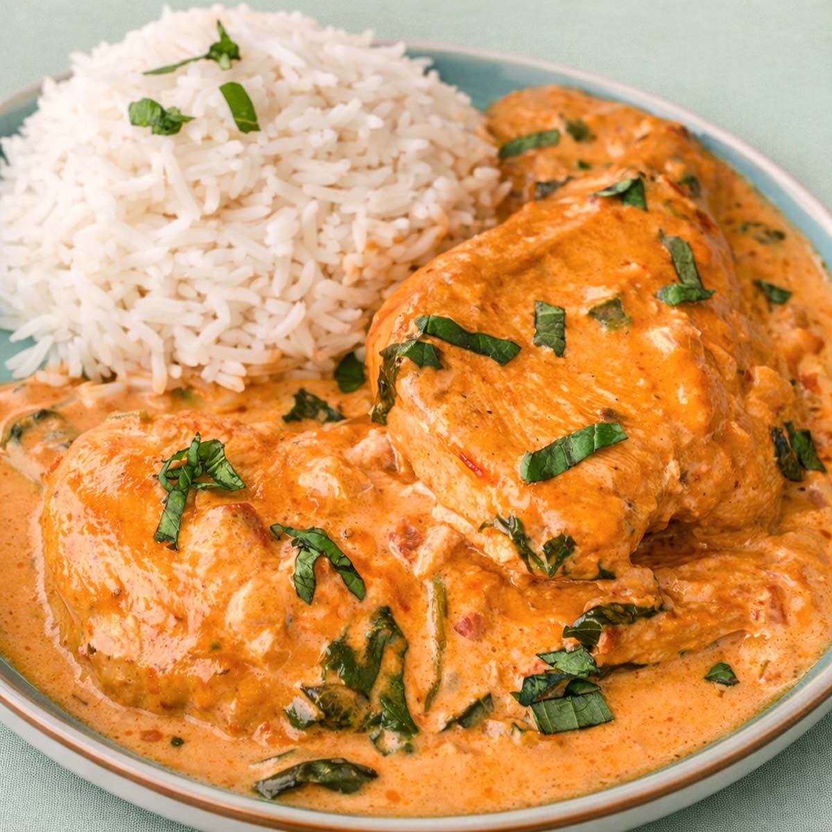 Creamy Tuscan chicken with sun-dried tomatoes and spinach served with fluffy white rice, garnished with fresh basil on a plate.