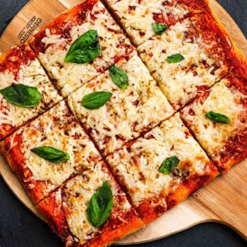 No Knead Pizza Dough baked into a crispy homemade sheet pan pizza with melted mozzarella cheese and fresh basil leaves