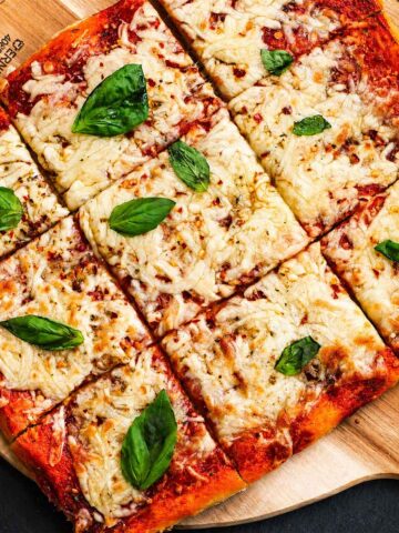 No Knead Pizza Dough baked into a crispy homemade sheet pan pizza with melted mozzarella cheese and fresh basil leaves