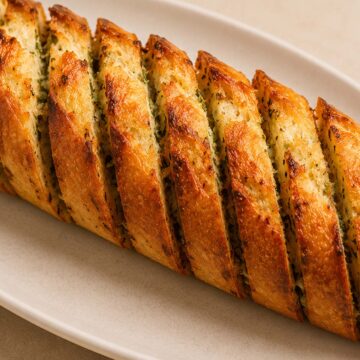 Golden crispy air fryer garlic bread on a ceramic plate with buttery garlic herb filling and toasted edges