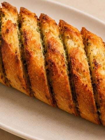 Golden crispy air fryer garlic bread on a ceramic plate with buttery garlic herb filling and toasted edges
