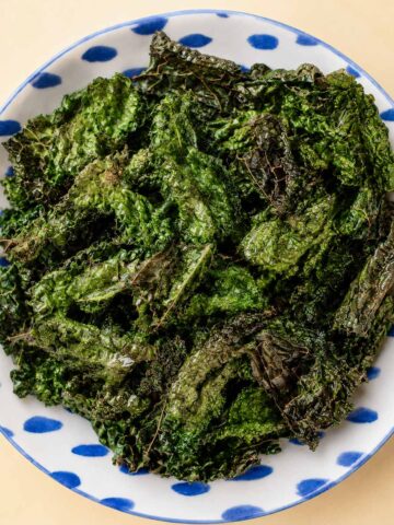 Air fryer kale chips served in a white bowl with blue details, showing crispy dark green kale leaves with crunchy edges.