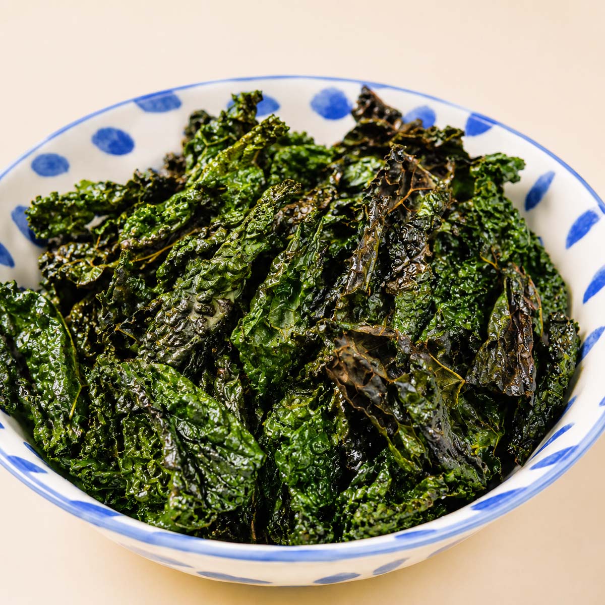 Close up air fryer kale chips served in a white bowl with blue details, showing crispy dark green kale leaves with crunchy edges.