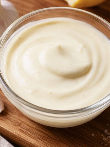 Homemade Spanish alioli recipe in a glass bowl with garlic cloves, creamy garlic aioli sauce