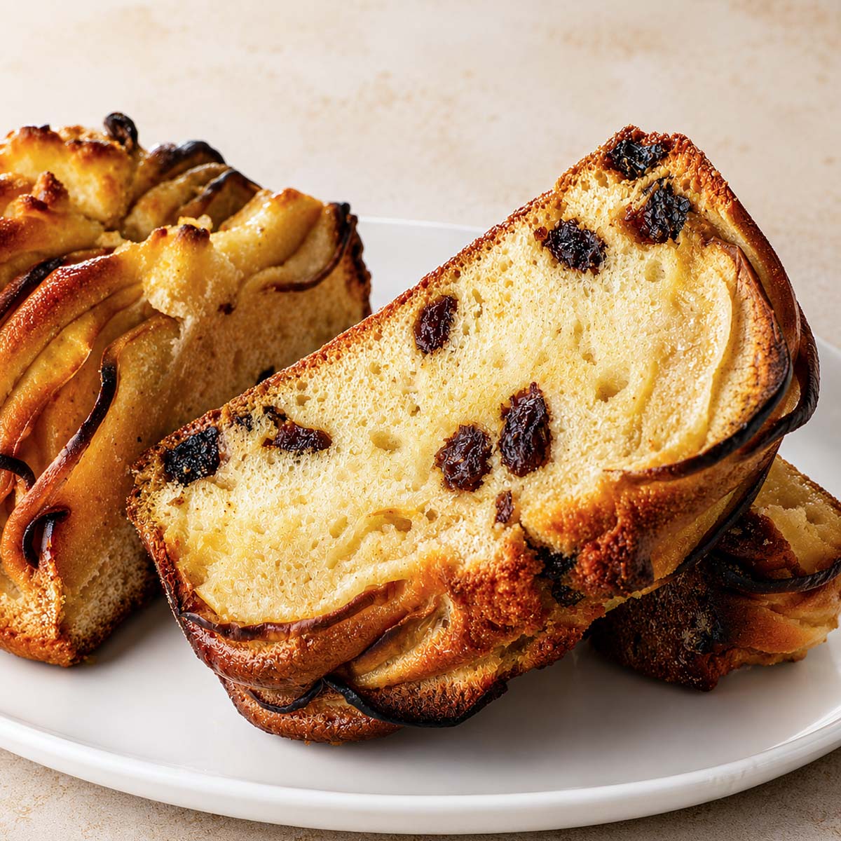 Apple loaf cake slice with raisins and baked apple layers on a white plate, featuring a golden crust and soft, buttery texture