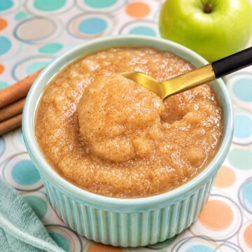 Creamy homemade apple sauce in a pastel blue ramekin with cinnamon and a golden spoon scoop.