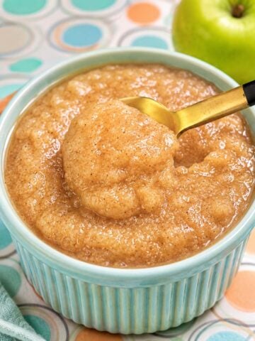 Creamy homemade apple sauce in a pastel blue ramekin with cinnamon and a golden spoon scoop.
