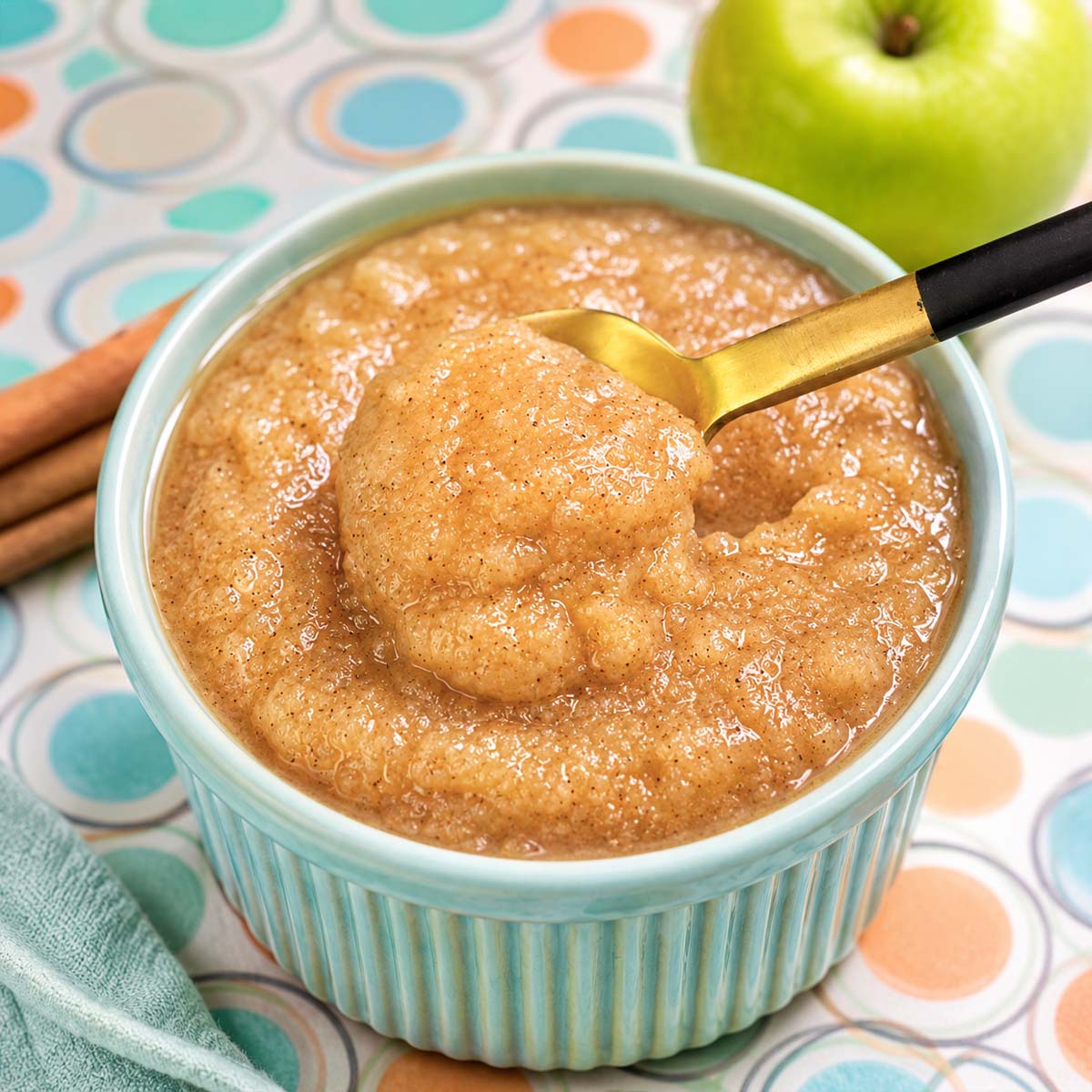 Creamy homemade applesauce in a pastel blue ramekin with cinnamon and a golden spoon scoop.