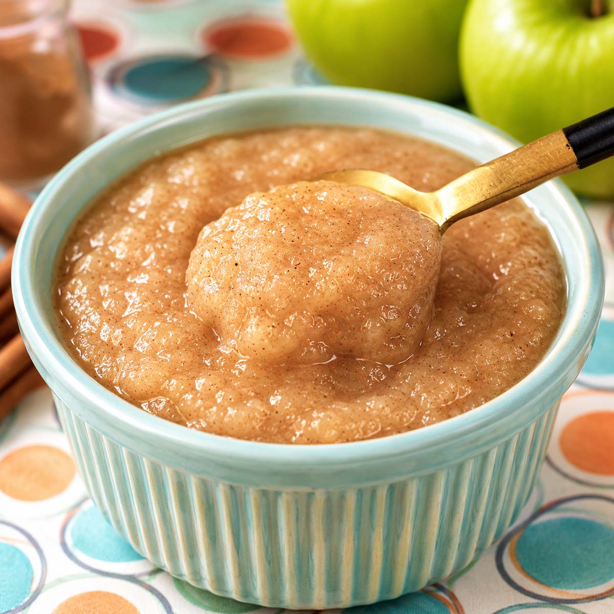 Close up Creamy homemade applesauce in a pastel blue ramekin with cinnamon and a golden spoon scoop.