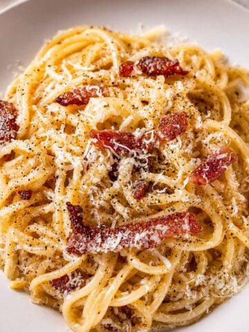 Creamy spaghetti carbonara topped with crispy pancetta, grated parmesan cheese, and black pepper