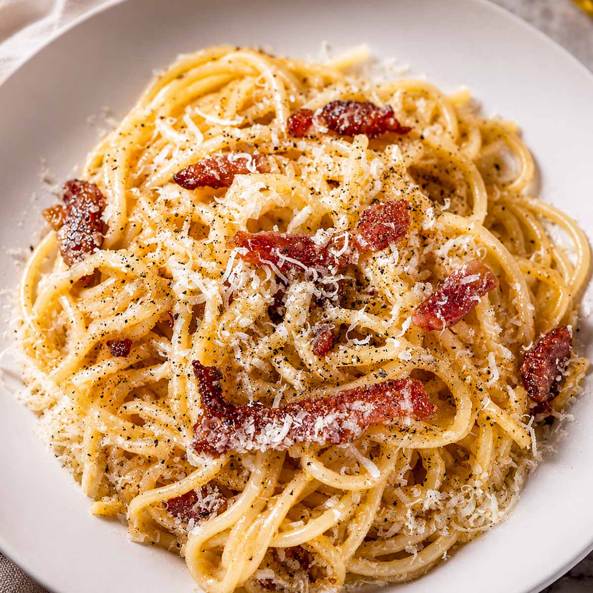 Creamy spaghetti carbonara topped with crispy pancetta, grated parmesan cheese, and black pepper