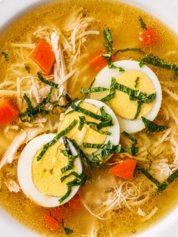 Chicken noodle soup with shredded chicken, carrots, thin noodles, and sliced boiled eggs in a clear golden broth
