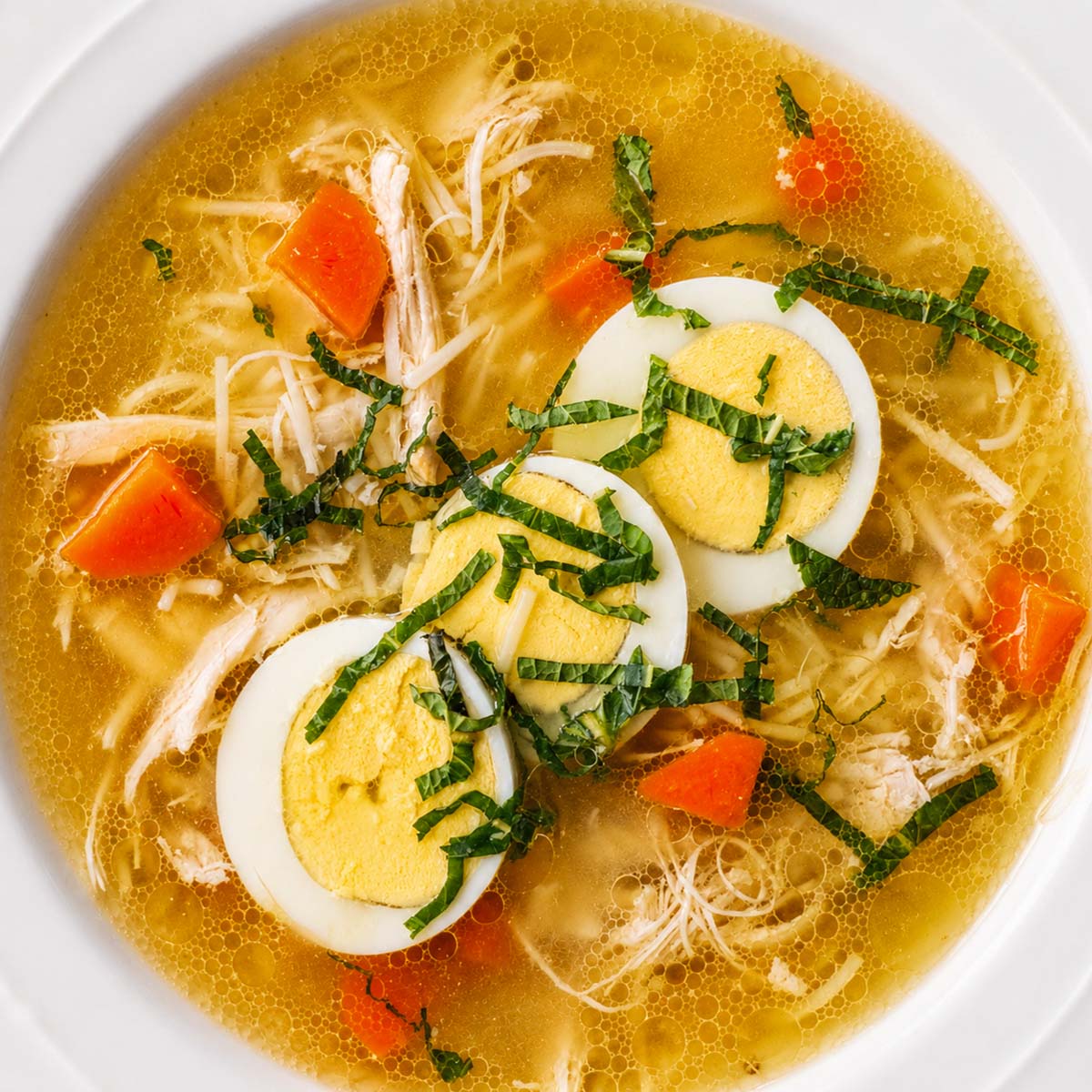 Chicken noodle soup with shredded chicken, carrots, thin noodles, and sliced boiled eggs in a clear golden broth