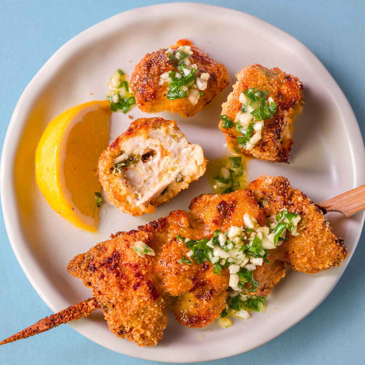 Lemon garlic butter chicken spiedini with crispy Parmesan breadcrumb coating, topped with garlic and parsley, served with a lemon wedge and sliced pieces showing the juicy inside.