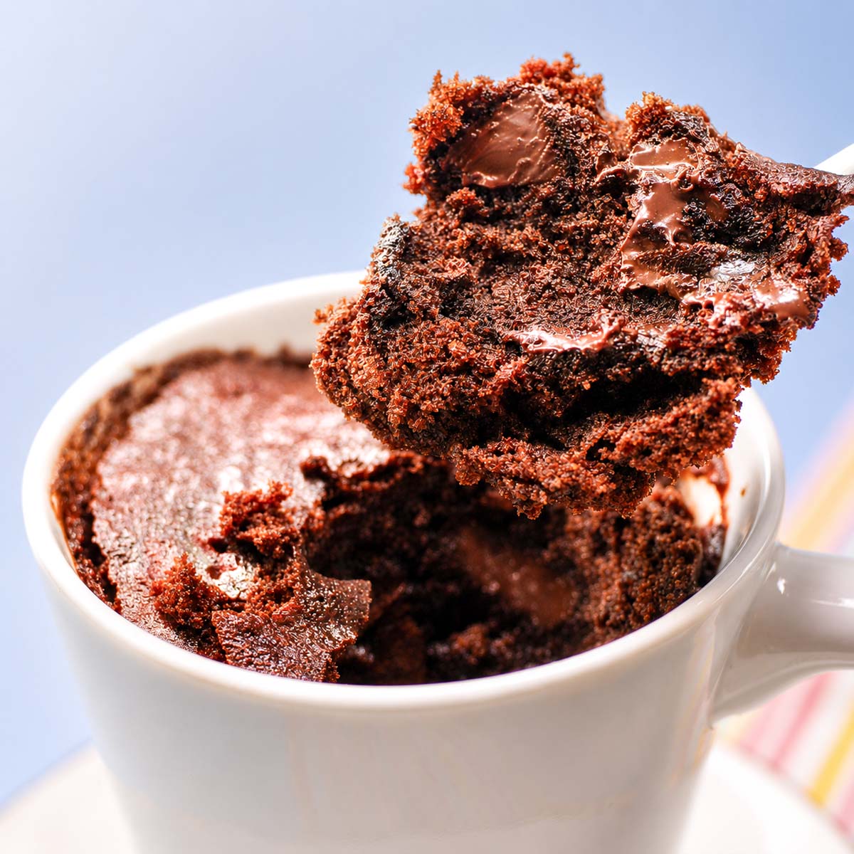 Close-up of a rich chocolate mug cake with a soft molten center being lifted from a white mug, showing the fudgy texture and airy crumb.