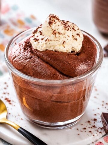 Chocolate mousse with cocoa powder topped with whipped cream and chocolate shavings in a glass dessert cup