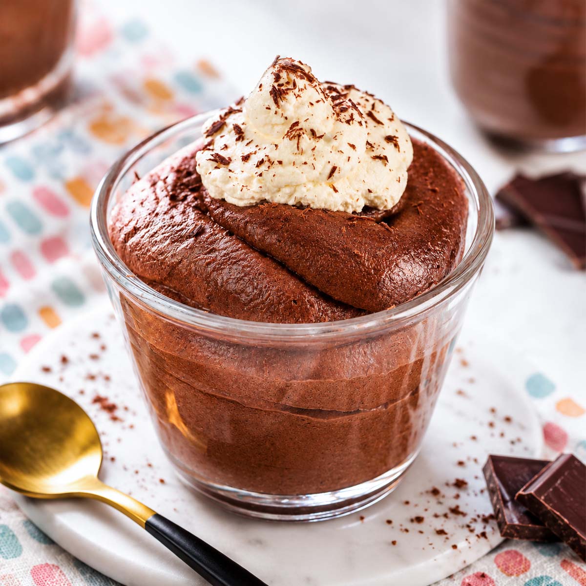 Chocolate mousse with cocoa powder topped with whipped cream and chocolate shavings in a glass dessert cup