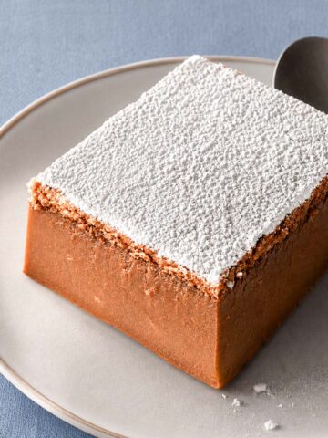 Coffee magic cake slice dusted with powdered sugar on a matte ceramic plate