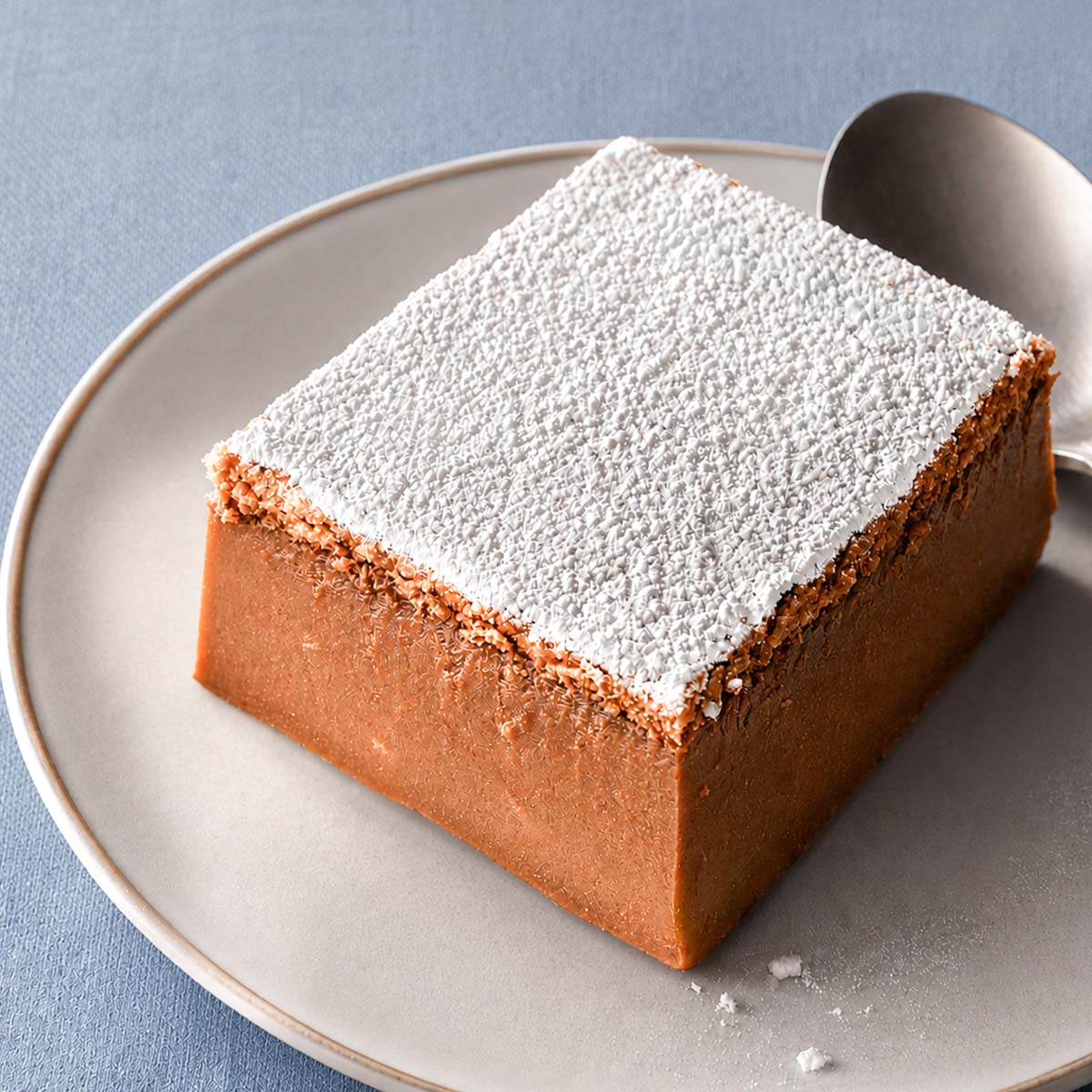 Coffee magic cake slice dusted with powdered sugar on a matte ceramic plate