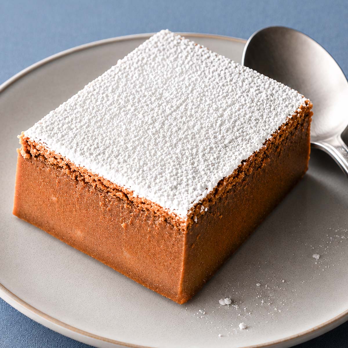 Close up coffee magic cake slice dusted with powdered sugar on a matte ceramic plate