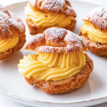 Easy cream puffs filled with vanilla custard on a white plate, dusted with powdered sugar