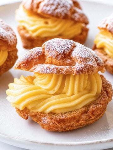 Easy cream puffs filled with vanilla custard on a white plate, dusted with powdered sugar
