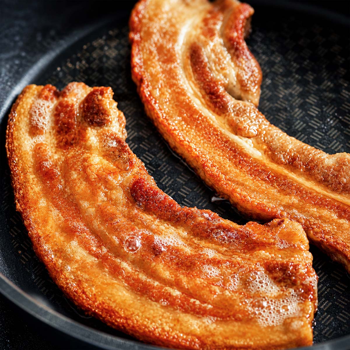 Crispy Pork Belly Chicharrones frying in a pan with golden, bubbly crackling and rich caramelized edges