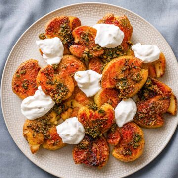 Crispy smashed potatoes with herb sauce and dollops of creamy yogurt on a plate