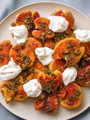 Crispy smashed potatoes with herb sauce and dollops of creamy yogurt on a plate
