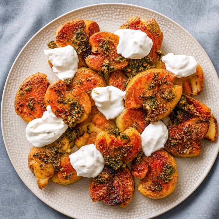 Crispy smashed potatoes with herb sauce and dollops of creamy yogurt on a plate