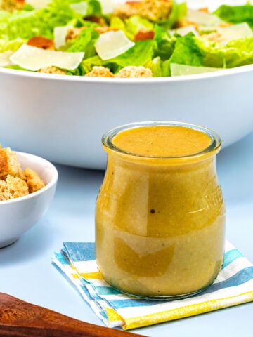 Easy Caesar Salad Dressing in a glass jar served with fresh romaine lettuce, croutons, and Parmesan