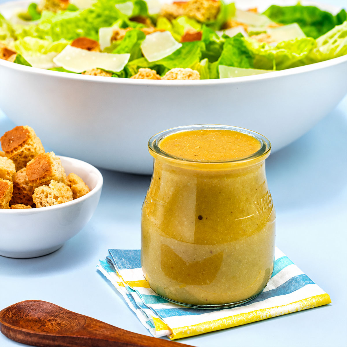 Easy Caesar Salad Dressing in a glass jar served with fresh romaine lettuce, croutons, and Parmesan