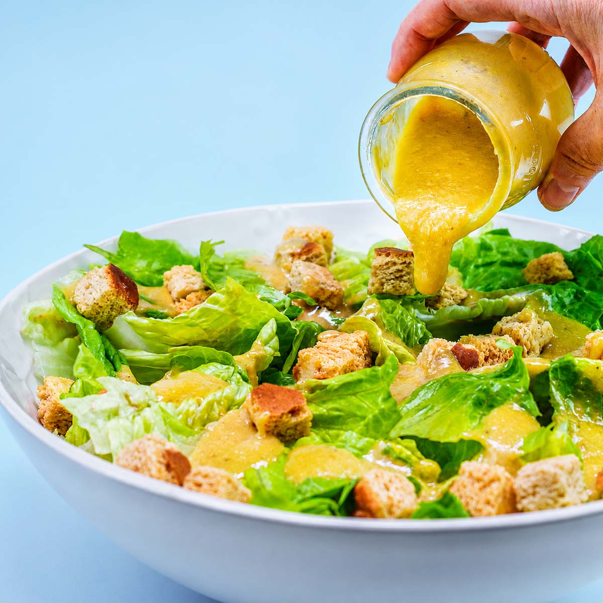 Easy Caesar Salad Dressing being poured over crisp romaine lettuce and crunchy croutons in a fresh homemade Caesar salad.