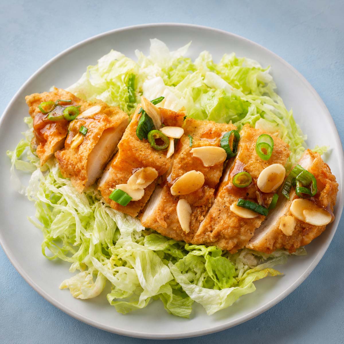 Crispy fried chicken breasts sliced over shredded lettuce with spring onions, almond flakes, and savory sauce