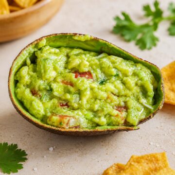 Easy Homemade Guacamole Recipe in an avocado shell with chunky avocado, tomatoes, and crispy tortilla chips