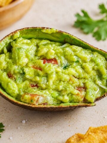 Easy Homemade Guacamole Recipe in an avocado shell with chunky avocado, tomatoes, and crispy tortilla chips