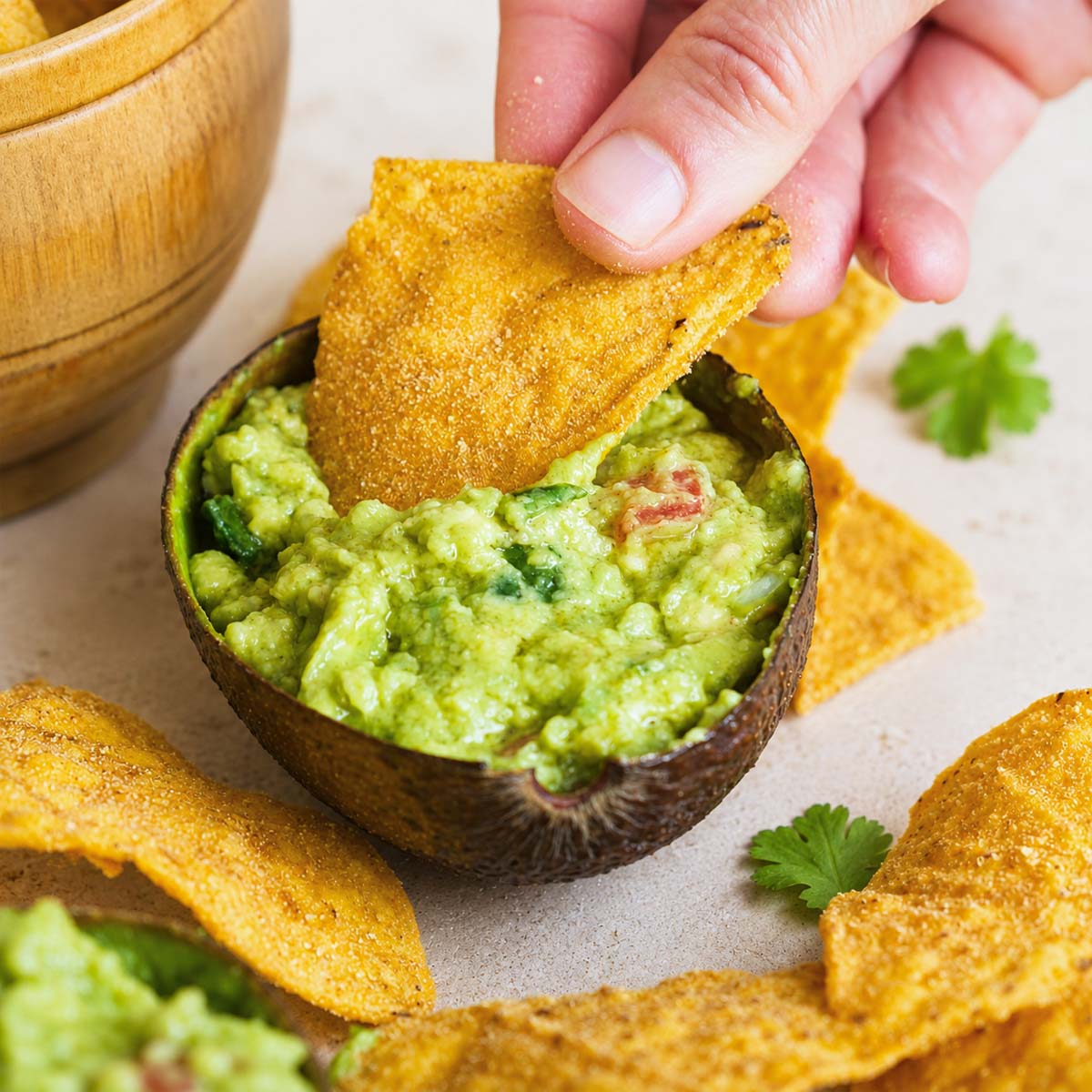 Easy Homemade Guacamole Recipe with crispy tortilla chips dipping into creamy avocado guacamole served in an avocado shell.