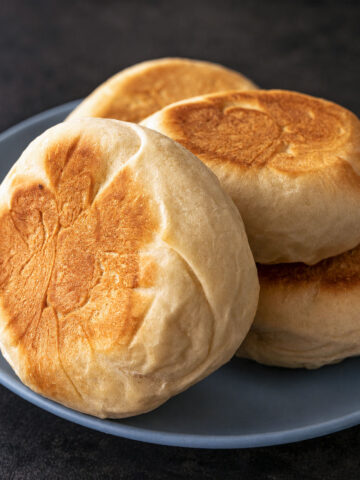 Homemade English muffins stacked on a blue plate with golden tops and a soft, fluffy texture, ready for breakfast or brunch.